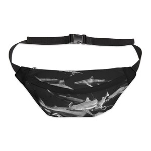May include: Black fanny pack with a white and gray shark print. The pack has a black adjustable strap.