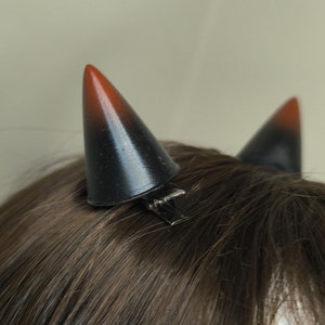 Op de afbeelding: Twee zwarte en rode duivelshoorn haarclips. De hoorns zijn puntig en hebben een zwarte clip aan de onderkant.