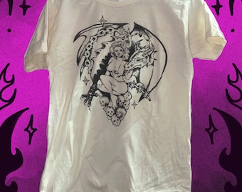 May include: A white t-shirt with a black and white graphic print of a woman sitting on a dragon with skulls and stars.