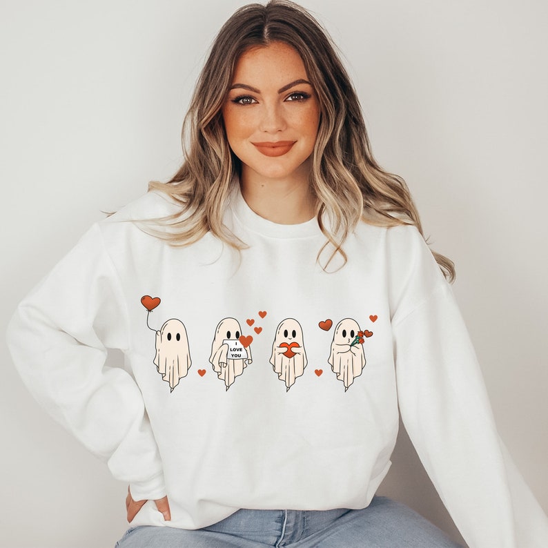 May include: White sweatshirt with a graphic of four ghosts holding hearts, balloons, and flowers. The ghosts are wearing red hearts and the text "Love You" is on one of the ghosts.