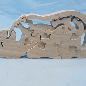 May include: A wooden puzzle in the shape of a train. The puzzle is made of multiple interlocking pieces that fit together to form the shape of a train. The puzzle is made of natural wood and has a light brown color.