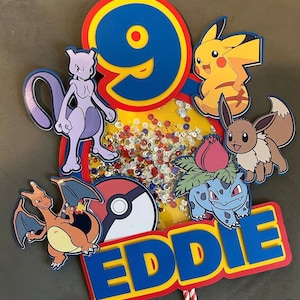 May include: A colourful cake topper featuring various Pokemon characters, including Pikachu, Eevee, Charizard, and Bulbasaur. The topper also includes a Pokeball, the number 9, and the name "EDDIE".