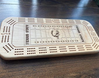 May include: A wooden cribbage board with a football field design. The board is engraved with the words "Ferris State" and features the school's bulldog mascot.