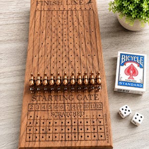 May include: A rectangular wooden horse racing board game featuring eleven bronze-colored horse figurines, a starting gate, a finish line, and a scratched section. The board includes numbered slots from 2 to 12, a deck of Bicycle playing cards, and two dice.