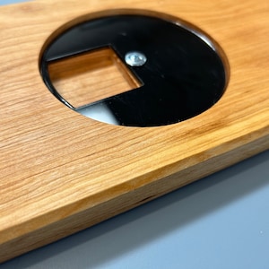 May include: A close-up of a wooden board with a circular cutout. The cutout is black and has a smaller rectangular cutout inside.