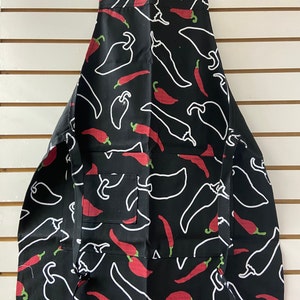 May include: Black apron with a white chili pepper pattern. The apron has a pocket and adjustable straps.