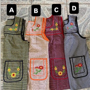 May include: Four sleeveless aprons labeled A, B, C, and D. Apron A is green plaid, B is beige plaid with orange trim, C is maroon, and D is blue plaid. Each apron features a front pocket and embroidered floral designs with yellow or red flowers.