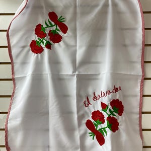 May include: White embroidered fabric with red flowers and the text "El Salvador" in red lettering. The fabric has a red and white checkered border.
