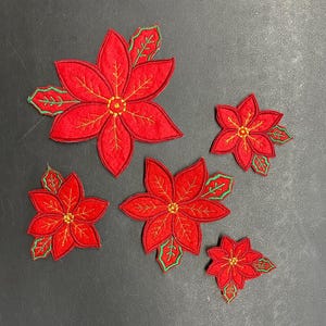 May include: Five red felt poinsettia flower appliques with green leaves and gold stitching. The appliques are different sizes.