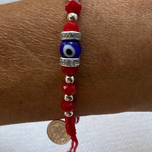 May include: Red string bracelet with a blue evil eye charm and silver beads. The bracelet has a silver coin charm at the end.