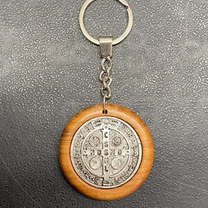 May include: A silver St. Christopher medal keychain with a wooden circle around it. The medal features a cross with the letters "INRI" and "NDSMD" on it.