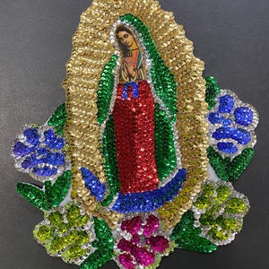 May include: A colorful, sequined appliqué featuring the Virgin Mary in a blue and red robe, surrounded by green and blue flowers. The appliqué is perfect for adding a touch of religious art to any project.