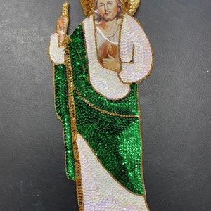 May include: A green and gold sequined religious icon depicting Jesus Christ. The icon is made of sequins and features a gold halo and a green robe.