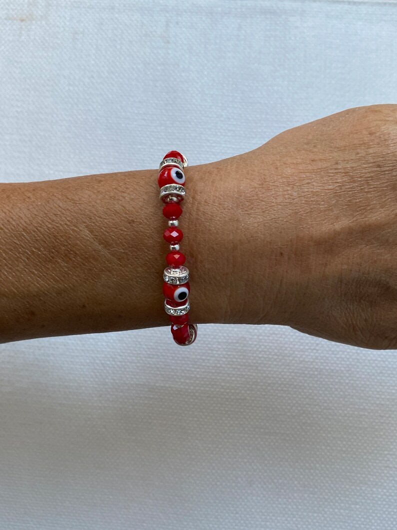 May include: Red beaded bracelet with silver charms and evil eye beads.