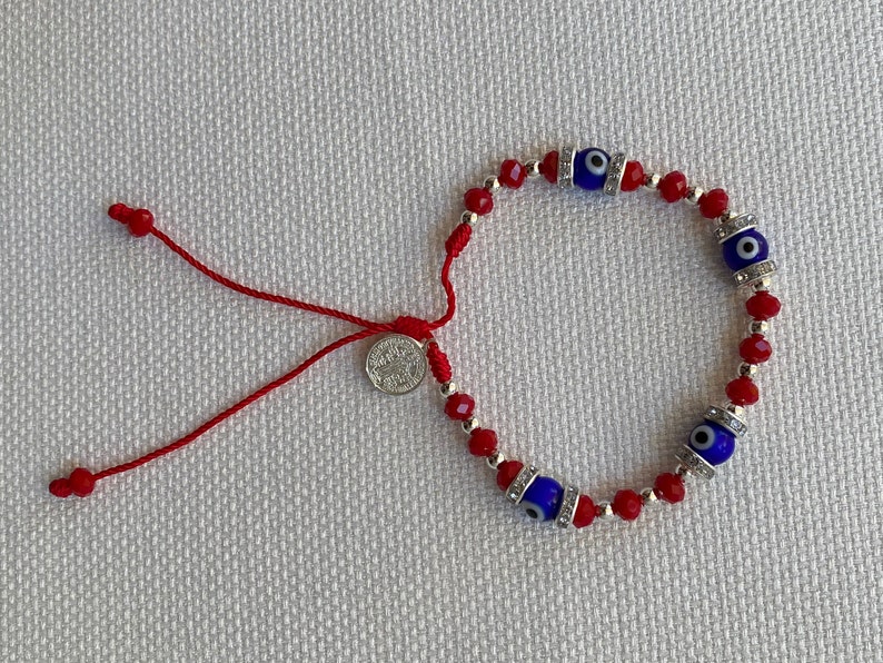 May include: Red string bracelet with blue evil eye charms and silver beads. The bracelet has a small silver charm with a religious image.