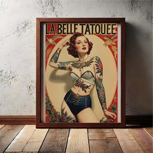 May include: A vintage-style poster with the text "La Belle Tatouee" in a red and gold frame. The poster features a woman with a colourful tattoo design on her body, wearing a blue and white swimsuit. The background is a red and gold design with birds.