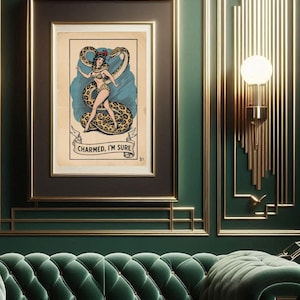 May include: Framed vintage-style print featuring a woman with a snake, with the text "CHARMED, I'M SURE". The artwork is in a black frame, set against a green wall with gold accents and a green velvet sofa.