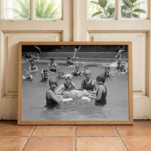 May include: Black and white framed photograph of a group of people in a pool. Several people are wearing swimsuits and swim caps. Some are holding a tray with items on it. The photograph is in a wooden frame.