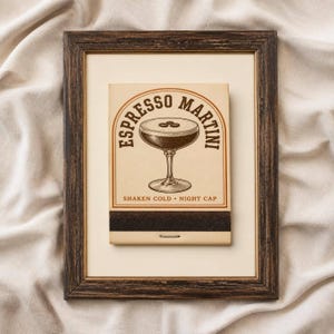 Op de afbeelding: Een rechthoekig luciferdoosje met een vintage-stijl illustratie van een espresso martini in een coupéglas met drie koffiebonen. De tekst luidt ESPRESSO MARTINI en SHAKEN COLD NIGHT CAP, ingelijst in een donkerbruine houten fotolijst.