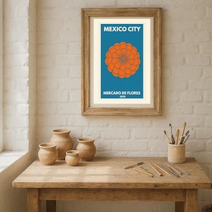 May include: A framed art print with the words "MEXICO CITY" above an orange flower design on a blue background. Below the flower, the text reads "MERCADO DE FLORES 1979". The print is in a wooden frame. There are several small clay pots on a wooden table.