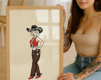 May include: A framed print featuring a cartoon cowgirl in a black hat with the text "Wild Thing." The cowgirl wears a red vest, brown pants, and red boots. The artwork has a vintage, pin-up style.