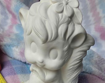 Könnte beinhalten: Eine weiße Eichhörnchen-Figur aus Keramik mit einer Blume auf dem Kopf, platziert neben einem gelben Maßband, das eine Höhe von etwa 19 cm anzeigt. Das Eichhörnchen hat große Augen, spitze Ohren und einen buschigen Schwanz mit matter Oberfläche.