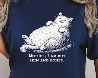 May include: Navy blue t-shirt featuring a relaxed white cat illustration. The cat is lying on its back with the text "MOTHER, I AM BUT SKIN AND BONES." This graphic tee is a comfortable and casual wear.