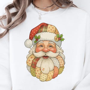 May include: White sweatshirt featuring a colorful Santa Claus graphic. The Santa design includes a patchwork hat and beard with holly accents. The Santa face is smiling with a rosy nose and cheeks, perfect for the holiday season.