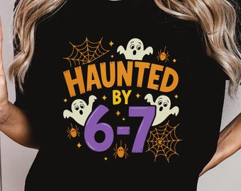 May include: Black t-shirt with a Halloween-themed design. The shirt features the words "HAUNTED BY" in orange, with the numbers "6-7" in purple. Ghost and spider web graphics complete the design.