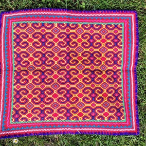 May include: A colourful woven tapestry with a geometric pattern in shades of red, yellow, blue, green, and white. The tapestry has a fringed border.