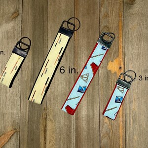 May include: Four key fobs on a wooden surface. Two are 3 inches long, and two are 6 inches long. One has a cream background with black text and orange lines. The other has a light blue background with red accents and a pattern.