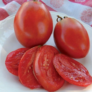 Puede incluir: Primer plano de tomates rojos maduros. Se muestran dos tomates enteros, junto con varias rebanadas. Los tomates tienen forma ovalada y una piel lisa y brillante.