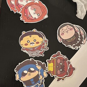 May include: A collection of colorful cartoon stickers featuring various animal characters. The stickers showcase a range of designs, including a fox, a tiger, a bunny, and other characters, each with unique outfits and expressions. The stickers are on a dark surface.