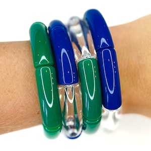 May include: A set of three bracelets, one clear, one green, and one blue. The bracelets are made of smooth, glossy material and are stacked on a person's wrist.