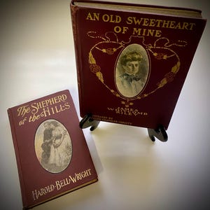 May include: Two vintage hardcover books with maroon covers and gold lettering. The book on the left is titled "The Shepherd of the Hiles" by Harold Bell Wright. The book on the right is titled "An Old Sweetheart of Mine" by James Whitcomb Riley, illustrated by Howard Chandler Christy.