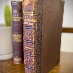 May include: Two brown leather-bound books with gold lettering. The book on the right has the title "I.C.S. Reference Library Drawing" and the text "By International Correspondence Schools Scranton, Pa."