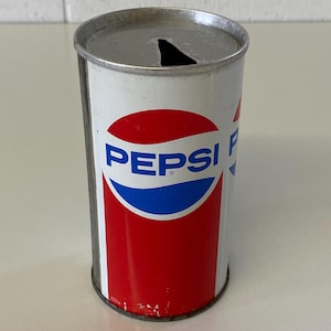 May include: Vintage Pepsi can with a white background, featuring the Pepsi logo in blue and red. The can has a silver top with a triangular opening. The can's design is a classic representation of the Pepsi brand.