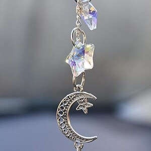 May include: A silver charm necklace featuring a crescent moon, star, and crystal accents. The charm hangs from a silver chain.