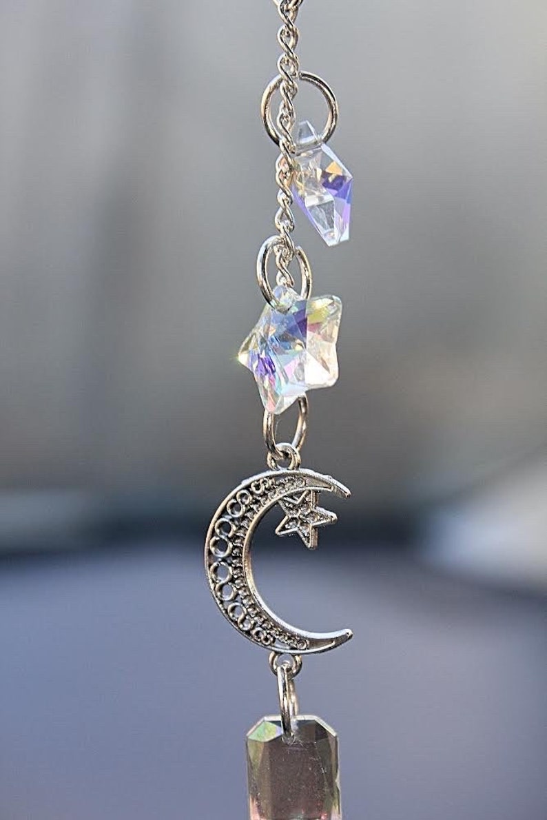May include: A silver charm necklace featuring a crescent moon, star, and crystal accents. The charm hangs from a silver chain.