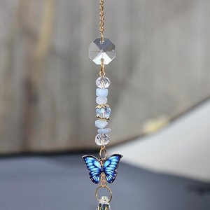 May include: A gold chain with a crystal prism, blue and clear beads, a blue butterfly charm, and a crystal teardrop hanging from it. This car charm is designed to catch the light and add a touch of sparkle to any vehicle.