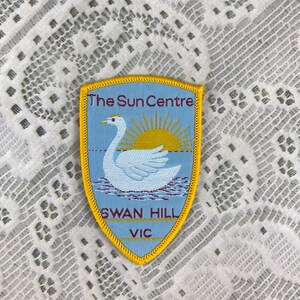 May include: A blue and yellow embroidered patch with the text "The Sun Centre" and "Swan Hill VIC". The patch features a white swan with a yellow sun in the background.