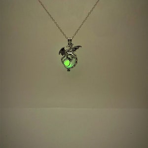 May include: A silver necklace with a dragon pendant. The dragon is holding a glowing green orb.