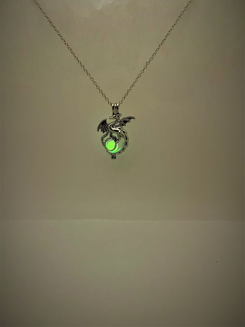 May include: A silver necklace with a dragon pendant. The dragon is holding a glowing green orb.