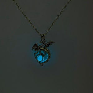 May include: A silver chain necklace with a dragon pendant. The pendant has a glowing blue orb inside.