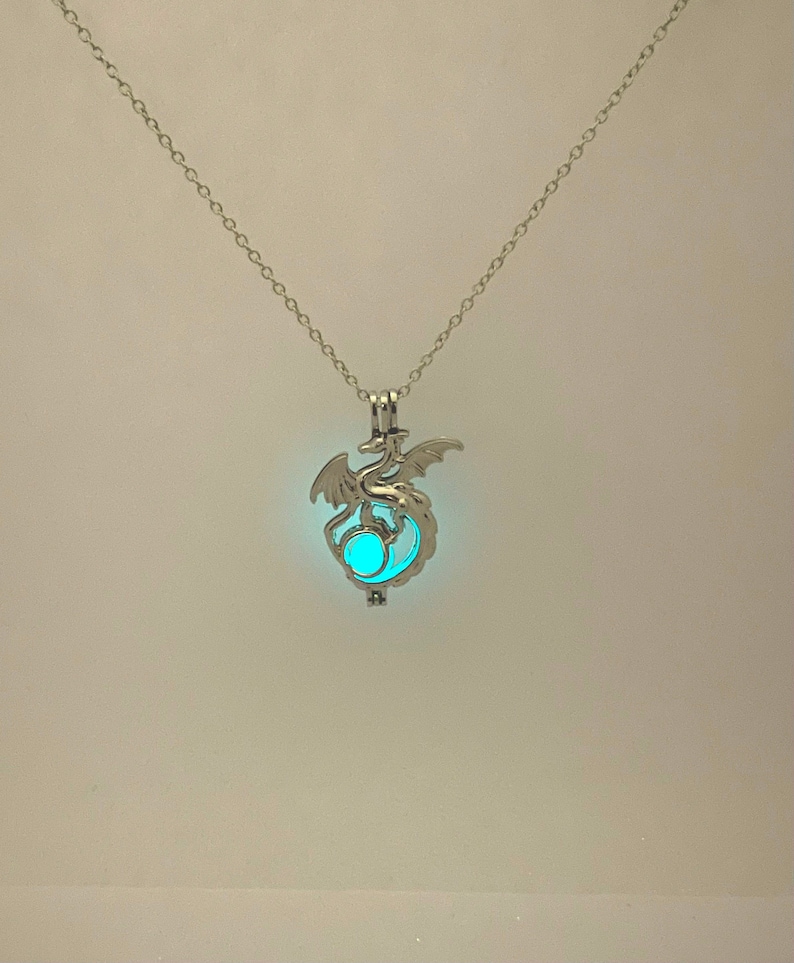 May include: A silver necklace with a dragon pendant. The dragon is holding a glowing blue orb in its claws.