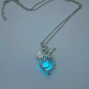 May include: A silver chain necklace with a pendant featuring a dragon holding a glowing blue orb.
