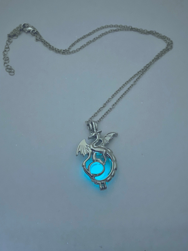 May include: A silver chain necklace with a pendant featuring a dragon holding a glowing blue orb.