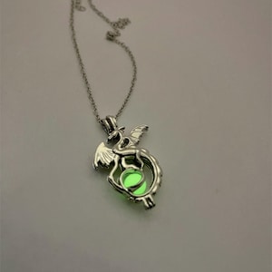 May include: A silver necklace with a dragon pendant. The dragon is holding a glowing green orb in its claws.
