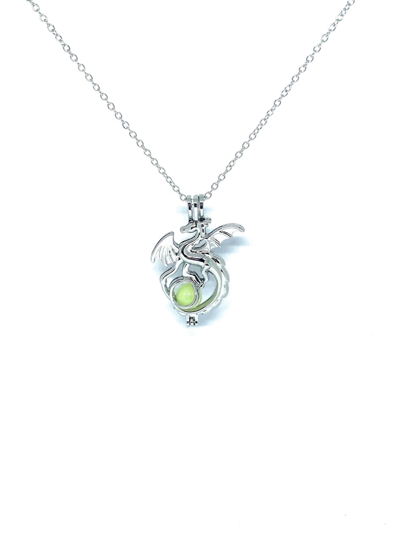 May include: A silver dragon charm necklace with a glowing green orb inside. The necklace has a delicate chain and a lobster clasp.