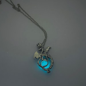 May include: A silver necklace with a dragon pendant. The dragon is curled around a glowing blue orb.